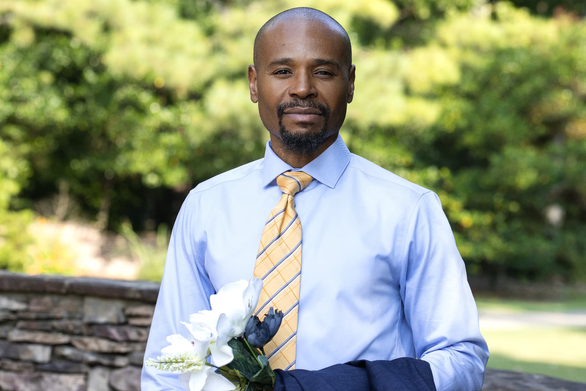 Moise (MO) Phanor outdoors in a light blue shirt and gold tie, smiling.
